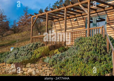 Braunes Holzhaus im nordischen Stil auf einem Hügel mit abwechslungsreichem Grün. Blauer Himmel und Sonnenlicht strömen am Frühlingstag ein Stockfoto