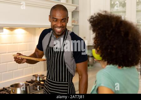 Fröhliches junges Paar, das in der Küche kocht und Schürze trägt Stockfoto