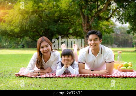 Asiatische Teenager Familie fröhlicher Urlaub Picknick-Moment im Park mit Vater, Mutter und Tochter liegen auf Matte und lächeln zu fröhlichen Urlaubszeiten zusammen Stockfoto