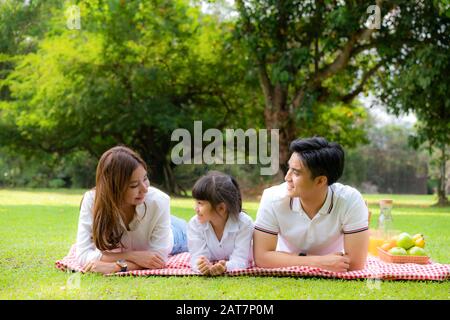 Asiatische Teenager Familie fröhlicher Urlaub Picknick-Moment im Park mit Vater, Mutter und Tochter liegen auf Matte und lächeln zu fröhlichen Urlaubszeiten zusammen Stockfoto