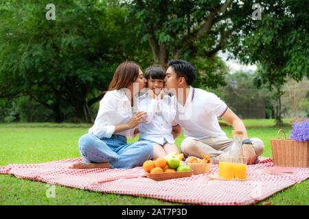 Asiatische Teenager Familie fröhlicher Urlaub Picknick-Moment im Park mit Vater, Mutter küssende Tochter mit Blick auf Kamera und Lächeln, um einen glücklichen Urlaub zu verbringen tim Stockfoto