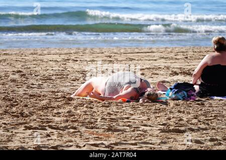 Benidorm, Provinz Alicante, Spanien. Januar 2020. Britische Touristen entspannen in der spanischen Sonne am Levante Strand und Promenade, Sonnenbaden. Stockfoto