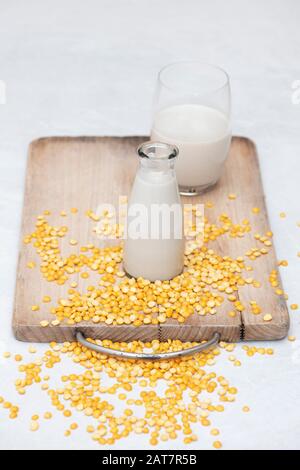 Vegane pflanzenbasierte Milchalternativen. Vegane Milchalternativen. Erbsenmilch mit gelb gespaltenen Erbsen auf einem Holzbrett Stockfoto