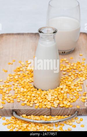 Vegane pflanzenbasierte Milchalternativen. Vegane Milchalternativen. Erbsenmilch mit gelb gespaltenen Erbsen auf einem Holzbrett Stockfoto