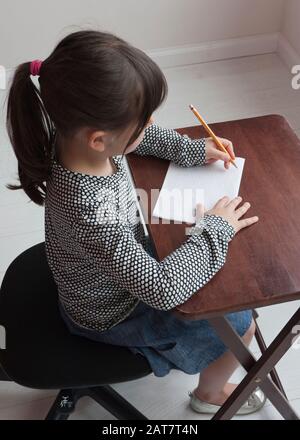 Das sechsjährige Mädchen sitzt an einem Schreibtisch und zeigt eine linkshändige Papierposition Stockfoto