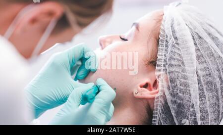 Die weibliche Kosmetikerin, die eine Injektion in junge Frau macht, ist mit dem Gesicht konfrontiert. Der Arzt Kosmetologe, der Gesichtskonturverfahren vorgeht. Konzept des Beauty-Salons Stockfoto