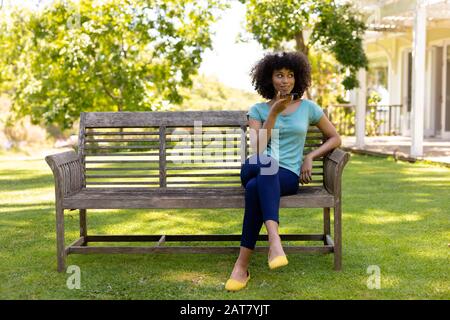 Junge Frau, die auf einer Bank im Garten sitzt Stockfoto
