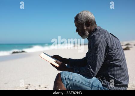 Alter Mann liest Buch am Strand Stockfoto