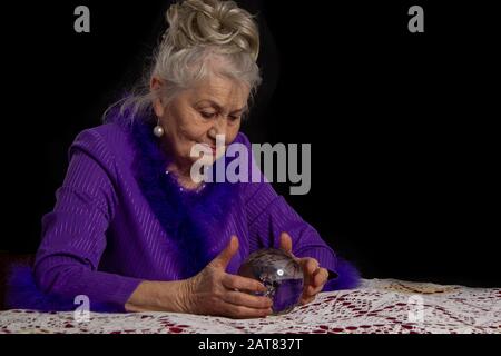 Betagte Zauberin mit Glaskugel. Fortuneteller bei der Arbeit. Stockfoto