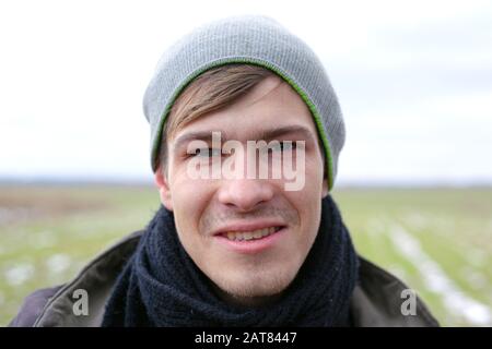 Junger, gutaussehender, unrasierter Kerl im Nahbereich mit Gesichtsporträt auf einem Frühlings-Feldhintergrund mit grünem Gras. Stockfoto