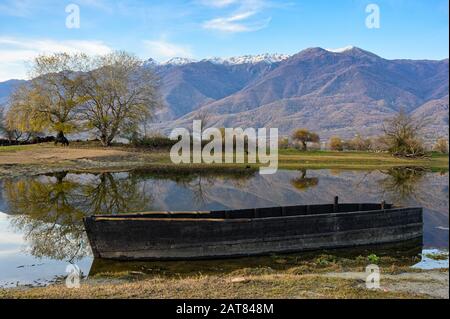 Blick auf Kerkini See im Norden Griechenlands ist mit traditionellen Holzmöbeln Fischerboot und Teil des schneebedeckten Mount Beles Stockfoto