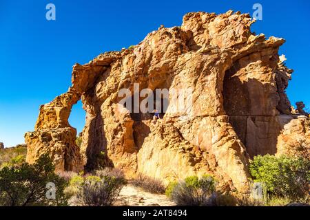 Spektakuläre Felsformation mit Bogen und Höhle, junge Frau auf einem freiliegenden Felsen sitzend, Stadsaal, Cederberg Wilderness Area, Südafrika Stockfoto