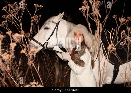 Hübsche junge Frau, die mit weißem Pferd spazieren geht Stockfoto