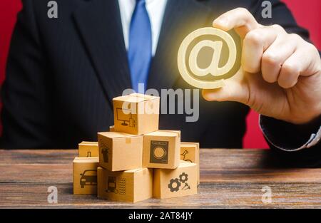 Der Geschäftsmann hält ein E-Mail-Internetsymbol über Boxen. Vertrieb Produkte online. Werbemarketing. Digitalisierung der Zollverwaltung Stockfoto