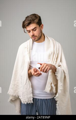 Junger Mann mit Decke, der einige Pillen zur Heilung seiner Krankheit nimmt Stockfoto