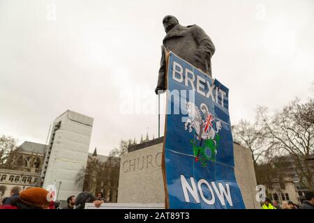 Westminster, London, Großbritannien. Januar 31, 2020. Ein großes blaues „BREXIT NOW“-Banner mit einem Löwen mit Union Jack-Schild ist auf dem Sockel der Winston Churchill-Statue am Parliament Square in London angebracht. Das Banner verdeckt teilweise Churchills Namen und symbolisiert eine durchsetzungsfähige Brexit-Stimmung. Blattlose Bäume und bewölkter Himmel deuten auf eine kalte Jahreszeit hin. Während Großbritannien die Europäische Union verlässt, gehen die Menschen auf die Straßen von Westminster und um das Parlament herum, um den Austritt zu feiern. Penelope Barritt/Alamy Live News Stockfoto