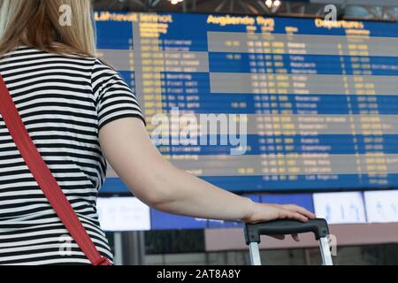 Frau schaut auf die Anzeigetafel am Flughafen. Wählen Sie ein Land für Reisen oder Migration aus. Stockfoto