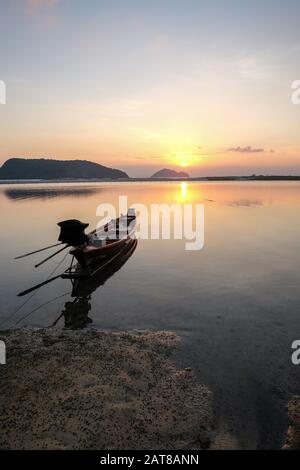 Boot auf dem Meer, umgeben von Felsen mit der Sonne Spiegelung auf dem Wasser während des Sonnenuntergangs Stockfoto