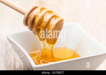 Nehmen Sie Honig aus einer weißen Schüssel mit Holz-Dipper. Stockfoto