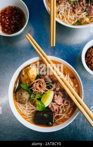 Großer Winkel nahe der Schüssel von Bun Bo Hue mit Rind, Krabbenkugeln, Blutwurst und Kräutern. Stockfoto