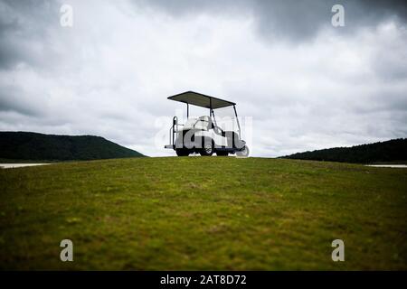 Golfwagen auf dem Grün eines Golfplatzes unter bewölktem Himmel geparkt. Stockfoto