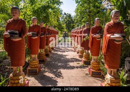 Reihe buddhistischer Monch-Statuen mit roten Gewändern und Almosenschüsseln in den Gärten des buddhistischen Tempels in Siem Reap Stockfoto