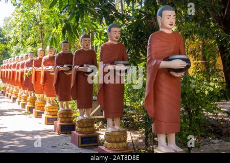 Reihe buddhistischer Monch-Statuen mit roten Gewändern und Almosenschüsseln in den Gärten des buddhistischen Tempels in Siem Reap Stockfoto