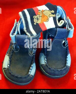 Süße blaue Babyschuhe und Socken auf Rot, Stockfoto