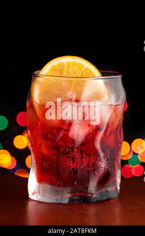 Bitterer Aperitif in einem Glas mit Eis und einer Orangenschicht mit bunten, entschärften Lichtern im Hintergrund Stockfoto