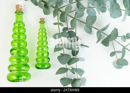 Glasgrüne Flaschen und ein Eukalyptuszweig auf weißem Grund. Eucalyptus ätherisches Öl für Spa. Stockfoto