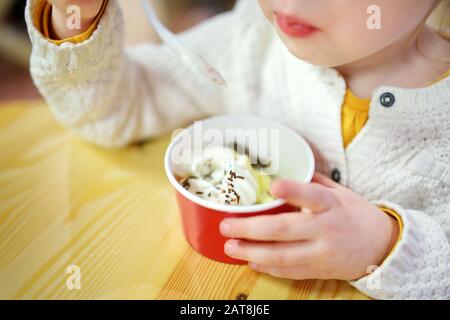 Süßes kleines Mädchen, das leckere frische Eiscreme im Haus isst. Kind, das Süßigkeiten isst. Süßes Essen für Kinder. Stockfoto