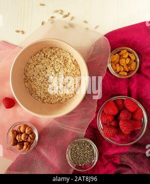 Superfood-Haferflocken in einer Schüssel mit Chia-Samen, Nüssen, Rosinen und Himbeeren auf Textilien auf hellem Holzhintergrund. Konzept der gesunden Ernährung und Ernährung Stockfoto