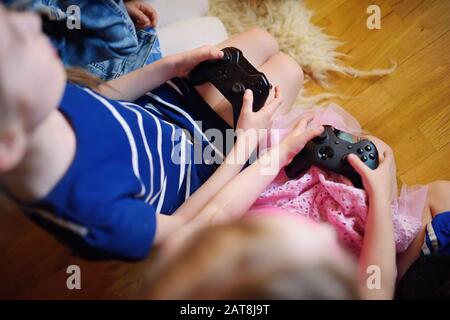 Zwei Schwestern spielen zu Hause Videospiele. Kinder, die Spaß haben, Gaming-Controller zusammen zu halten. Familienurlaub und Spaß im Innenbereich. Stockfoto