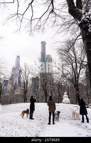Schneebedeckter Morgen in New York, Midtown Manhattan. Menschen, die ihre Hunde im Central Park spazieren gehen, genießen und einen Schneemann betrachten. Stockfoto
