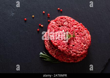 Lebensmittelkonzept Bio roh Hackbrasen oder gemahlenes Rindergras füttern Burger auf schwarzem Schieferstein mit Kopierraum Stockfoto