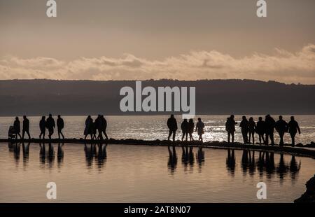 Menschen, die auf der Wirral-Halbinsel bei West Kirby auf dem Meeressee spazieren, untergehen bei Sonne auf dem Wandpfad zwischen Bootssee und der Dee-Flussmünde Stockfoto