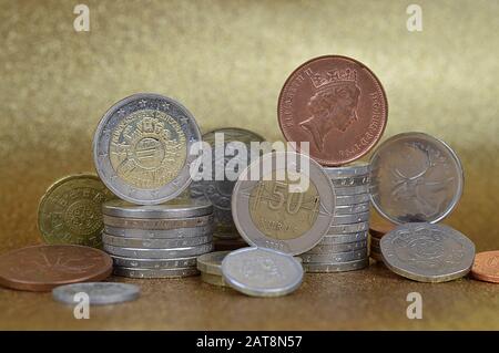 Münzstapel aus verschiedenen Nationen mit Euro und Cent vor goldenem Hintergrund Stockfoto