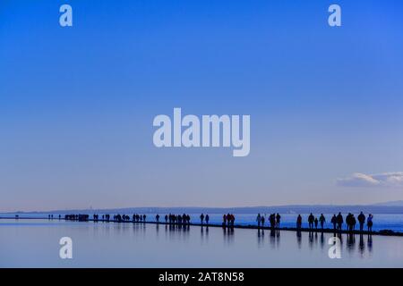 Menschen, die im Winter auf der Halbinsel Wirral auf dem Meeressee bei West Kirby auf dem Wall Path zwischen Bootssee und der Flussmünde der Dee spazieren gehen Stockfoto