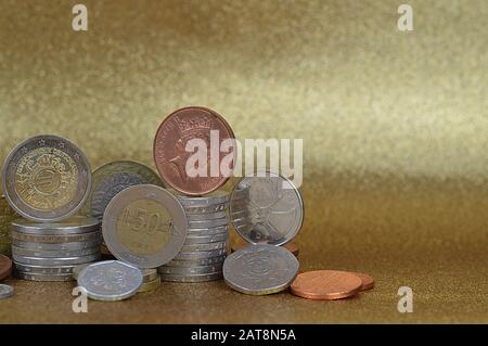 Münzstapel aus verschiedenen Nationen mit Euro und Cent vor goldenem Hintergrund mit Kopierraum rechts Stockfoto