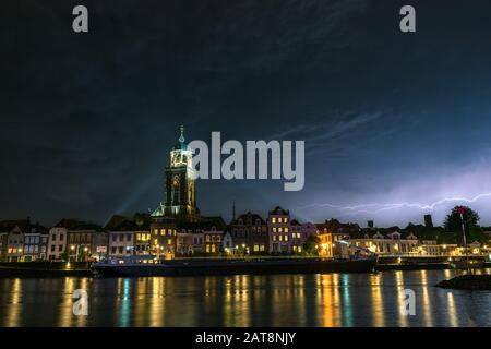 Schöner Blick auf die Stadt Deventer, Niederlande bei Nacht mit bunten Reflexionen im Wasser des Flusses. Blitz über der Skyline der Stadt Stockfoto