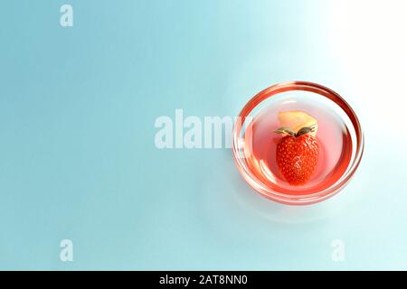 Gelee mit Erdbeere in Form eines Herzens auf blauem Hintergrund, das von einem Lichtstrahl auf der rechten Seite beleuchtet wird. Stockfoto