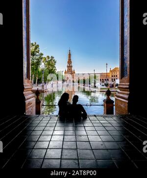 Silhouetten junger Paare, die den Sonnenuntergang auf dem berühmten spanischen Platz (Plaza de Espana) genießen. Sevilla, Spanien. Stockfoto