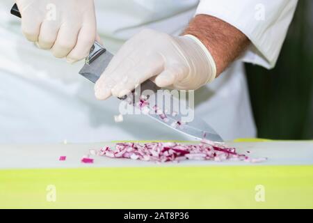 Der Küchenchef entfernt frisch geschnittene rote Zwiebelwürfel aus einem Messer in ein Schneidebrett. Kochkonzept. Stockfoto