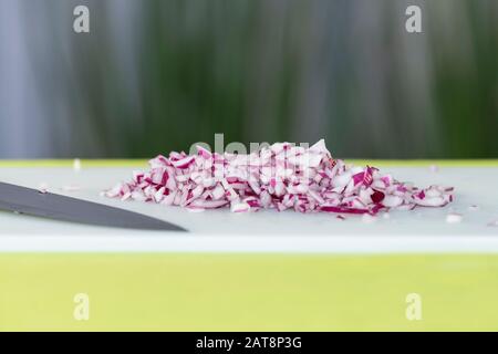 Schmackhaft aussehender, frisch geschnittener roter Zwiebelwürfel neben einem Messer auf einem Schneidebrett auf einem unscharf abgespeckten Hintergrund. Kochkonzept. Stockfoto