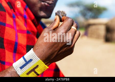 Afrikanischer Mann, der einen schwelenden Kuchen in der Hand mit farbenfrohem Armband hält. Tansania, Afrika. Stockfoto