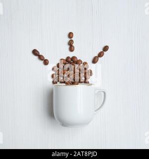 Abstrakte Sonne aus Kaffeebohnen und einer weißen Tasse auf Holzgrund. Draufsicht. Stockfoto