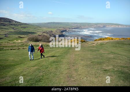 Ein älteres Paar, das auf dem Cleveland Way über Robin Hood's Bay, North York Moors National Park, Yorkshire, England, Großbritannien spazieren geht. Stockfoto