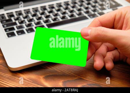 Eine Hand hält eine Kreditkarte vor einem Laptop. Platz für Text und Grafiken. Verspotten Sie sich. Nahaufnahme. Stockfoto