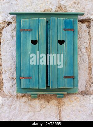 Ein herzförmiges Loch in den malerischen blauen Holzfenstern am Fenster eines alten kroatischen Steinhauses. Romantisches Bild für Valentinstag Stockfoto