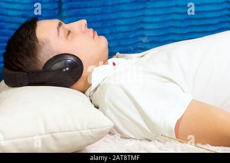 Ein junger Mann in einem weißen T-Shirt zu Hause, der entspannende Musik hört. Entspannung, Ruhe Stockfoto